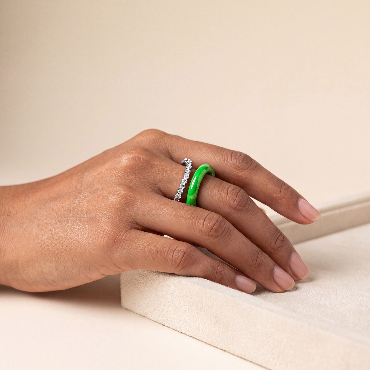 Green pavé infinity ring worn on the hand: a fine row of stones beside a glossy green enamel band